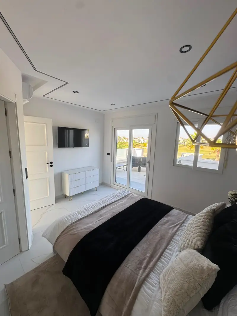 Master bedroom with king bed, geometric gold pendant and patio doors onto the terrace overlooking the fairway