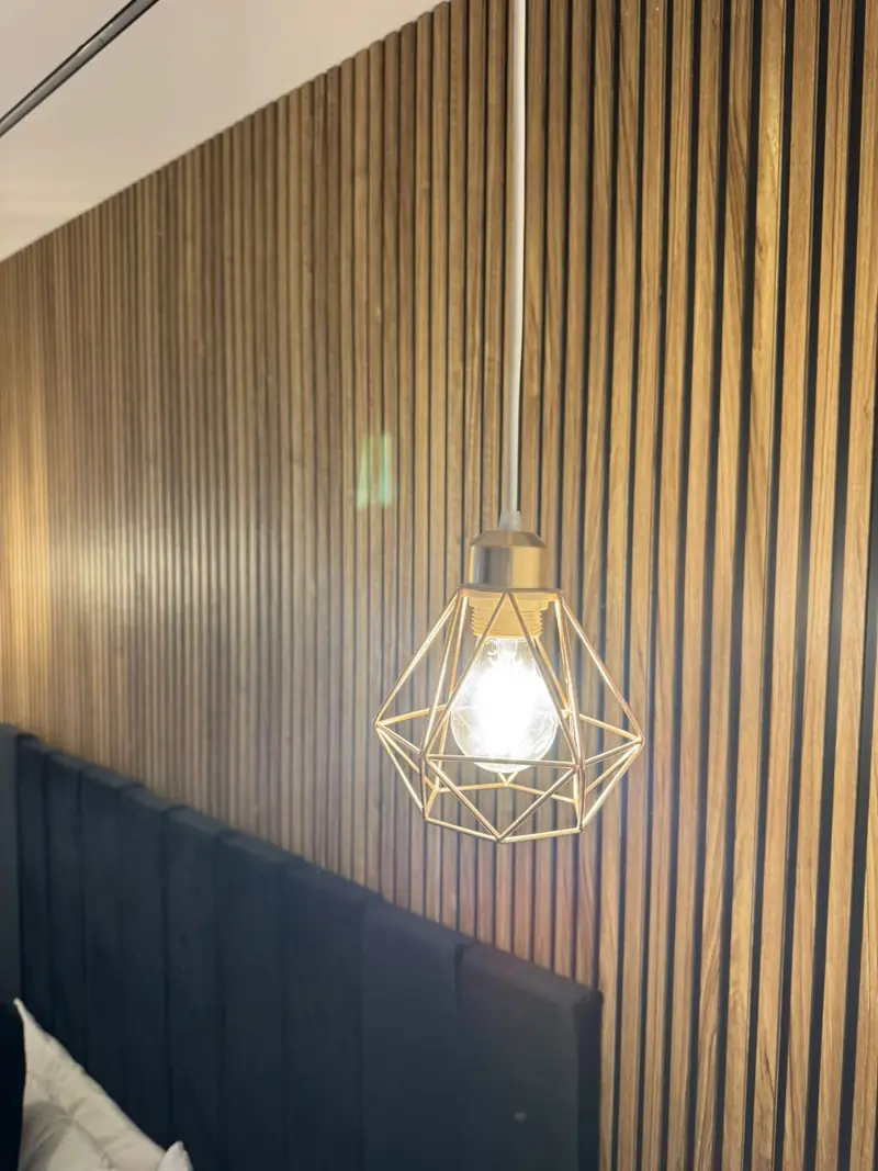 Close-up of the second bedroom's gold cage pendant light against the walnut slatted feature wall