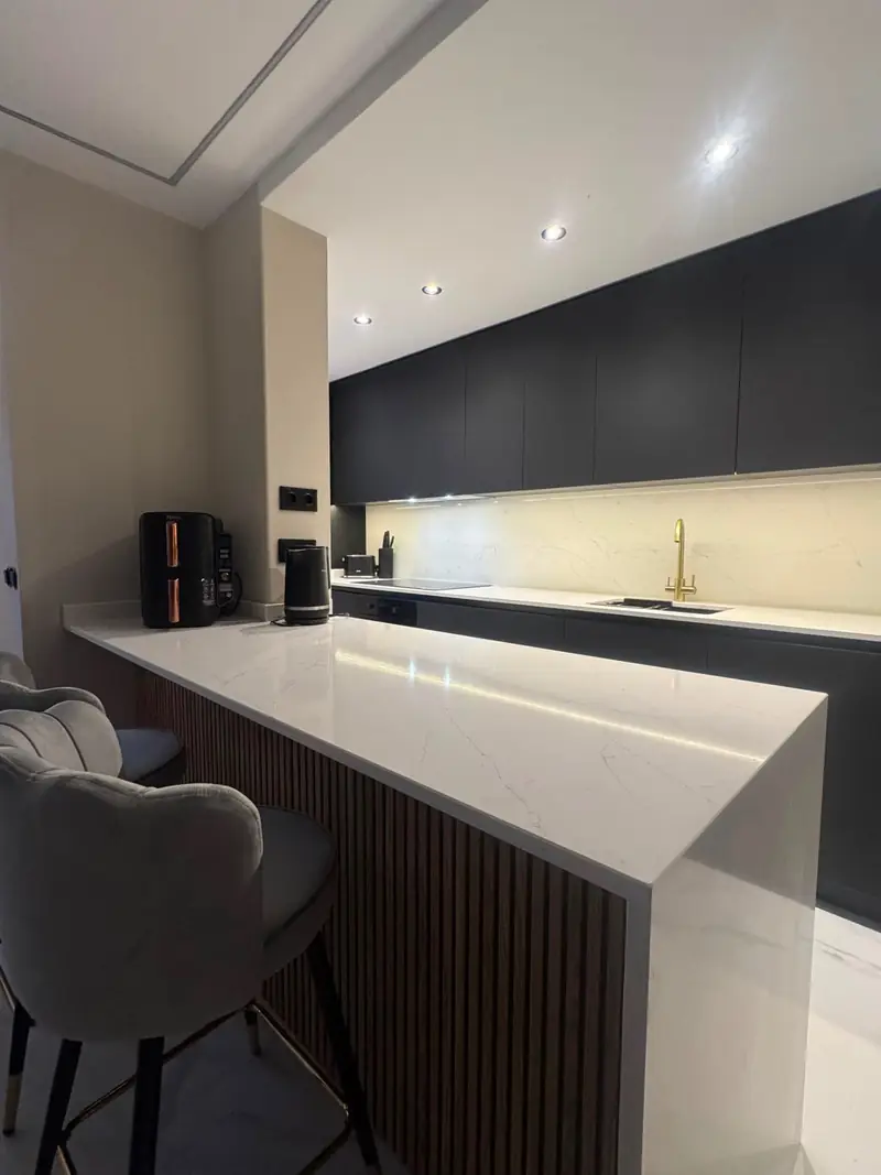 Sleek black-cabinet kitchen with white marble breakfast bar, brass tap and velvet bar stools