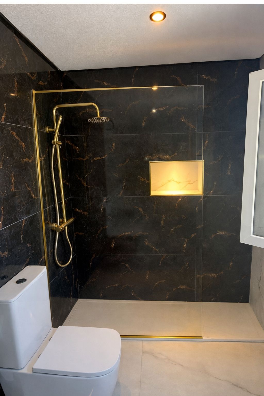 Walk-in shower with black marble tiling, brass rainfall shower and lit alcove niche