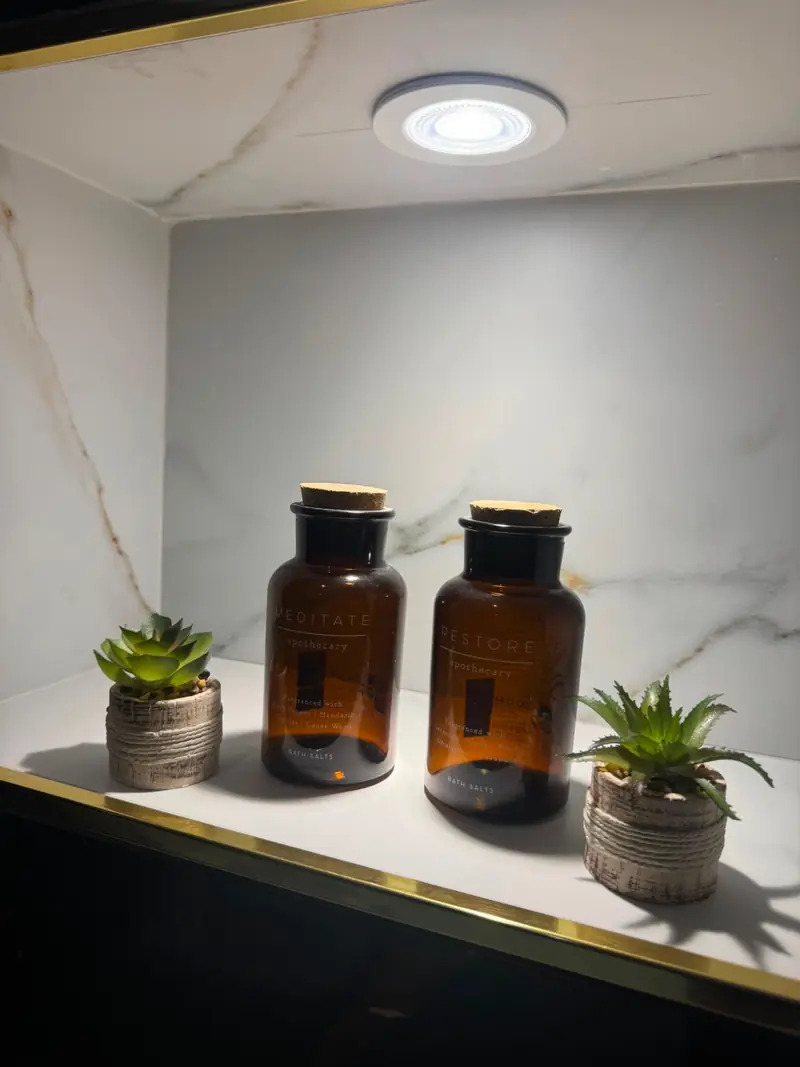 Lit brass-framed shower niche styled with amber apothecary bottles and small succulents