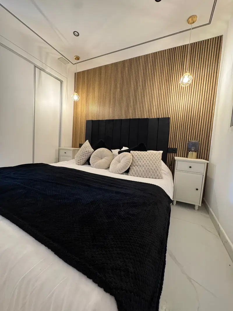 Second bedroom with black velvet headboard, walnut slat feature wall and twin geometric gold pendant lights