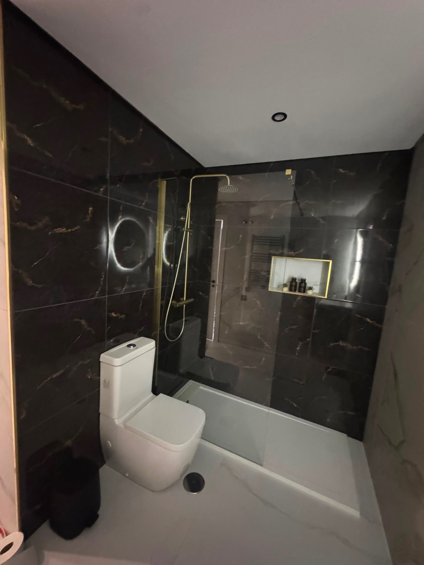 Wide view of the en-suite with black marble walls, walk-in shower and brass-framed niche